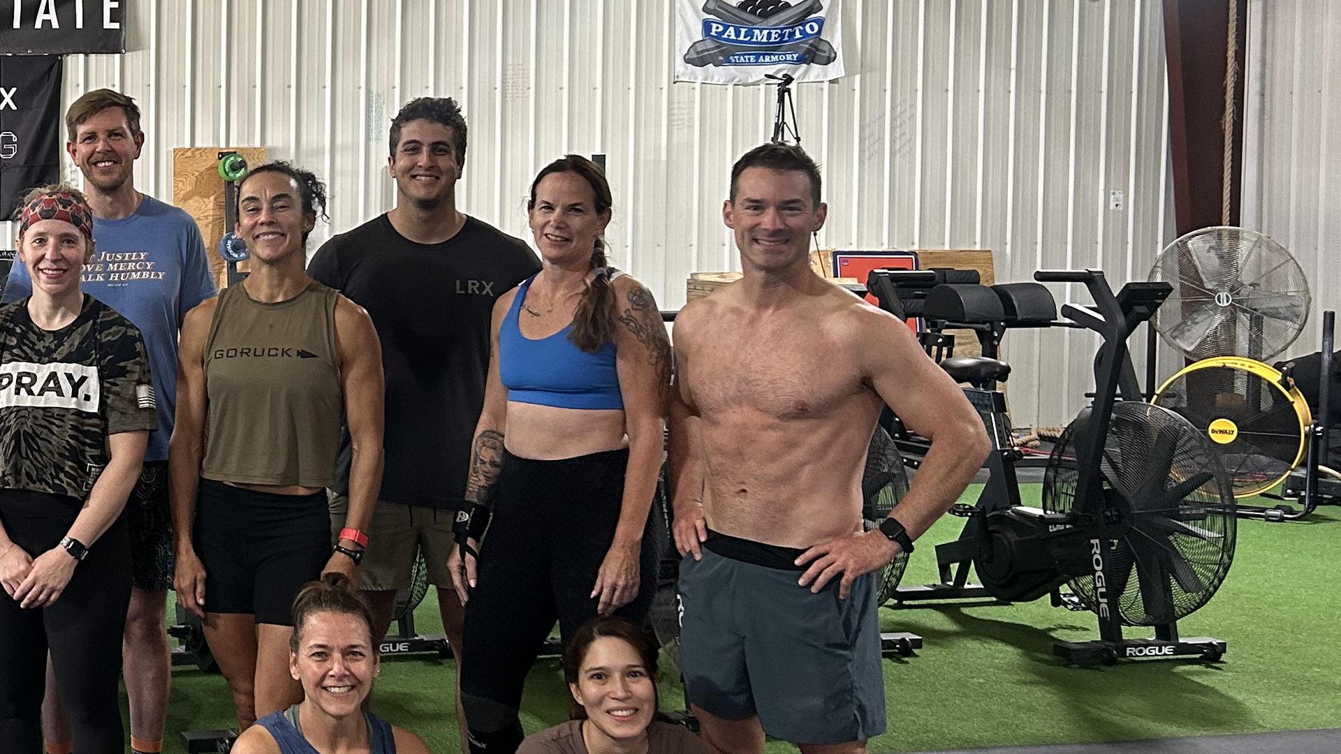 Athletes pose together in two rows on the gym floor, with exercise bikes behind them.