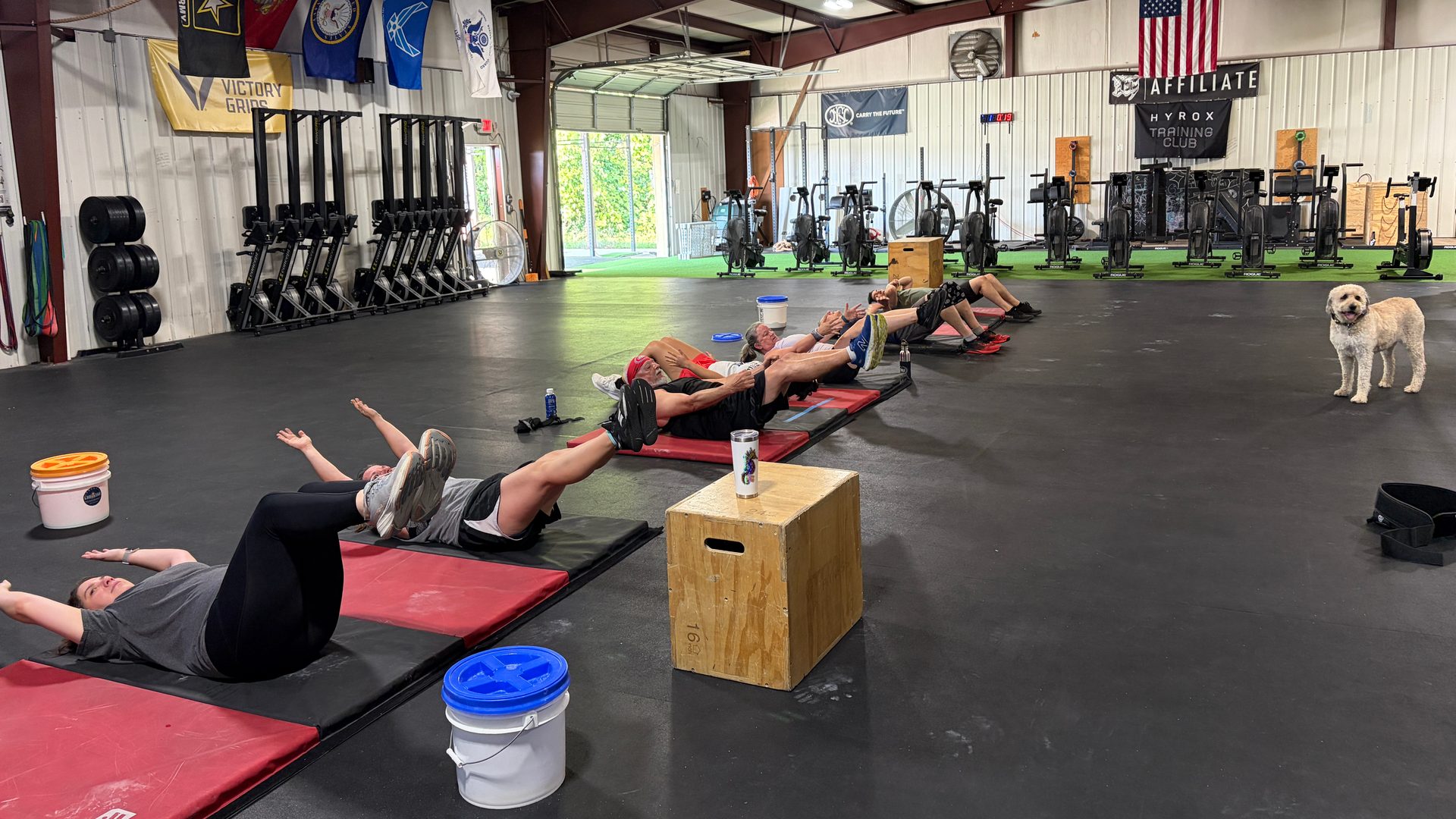 A class lying on mats working through core holds, rowers and service flags along the wall behind them